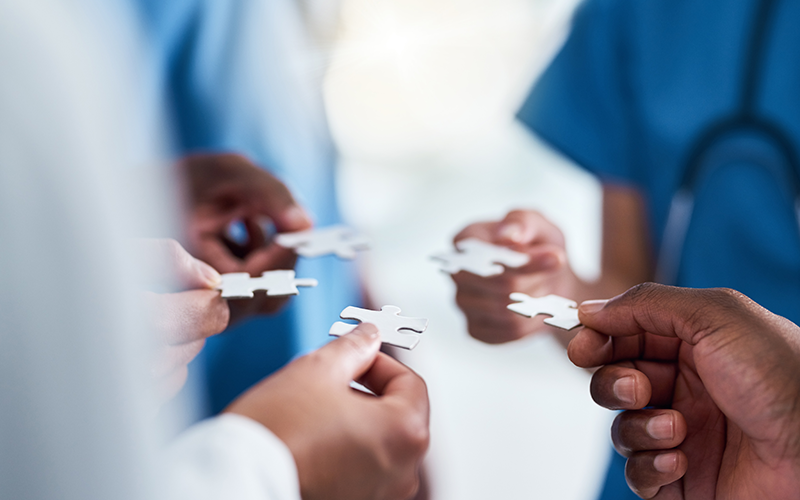 Hands of five hospital clinicians putting puzzle pieces together