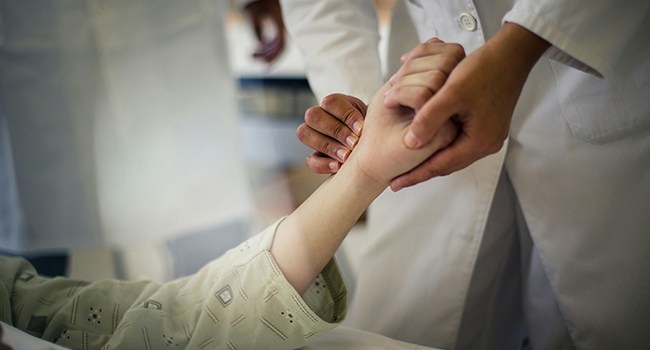 A doctor's hands holding a young hospital patient's hand as he check pulse in a very caring gesture